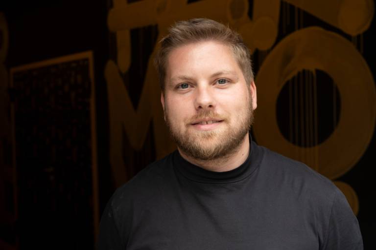 Wolfgang Hingerl stands in front of a dark wall and smiles into the camera.