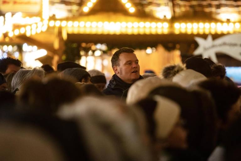 Visitors of the Christkindlmarkt under festive lighting.