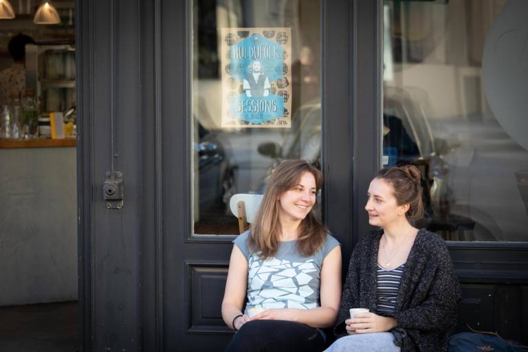 Stephanie Bjarnason and Anika Landsteiner sitting in front of a café.