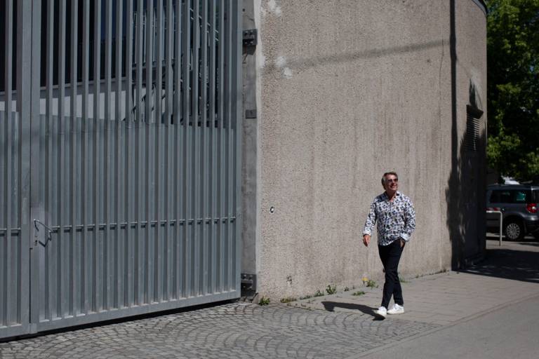 A man in sunglasses walks along a wall in Munich and laughs.