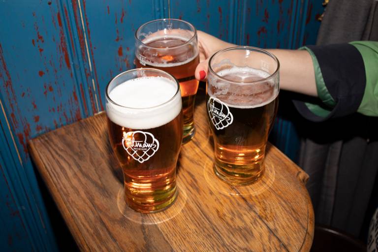 Three beer glasses on a wooden table at the bar "Frisches Bier" in Munich and a person reaches for them.