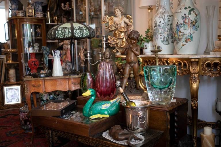 Antique statues and vases stand amidst antique furniture and old lamps
