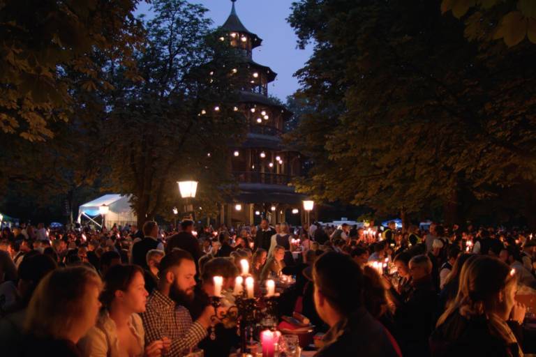 Guests at the Kocherlball sit at beer tables during dawn in Munich.