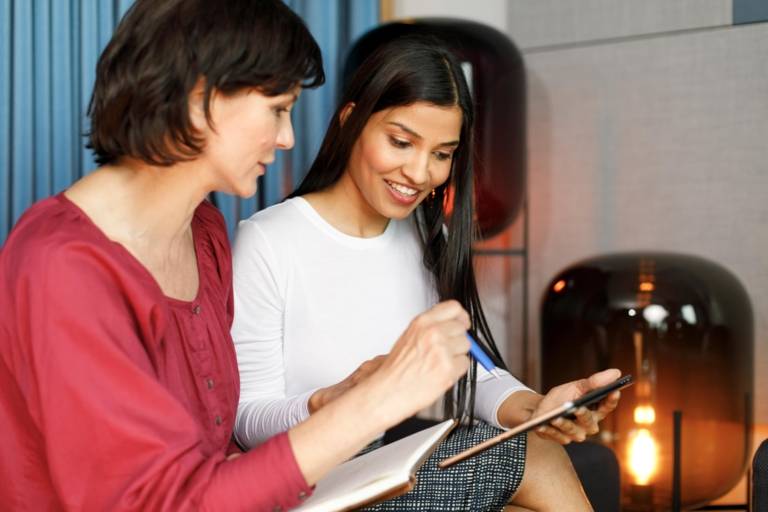 Zwei Frauen diskutieren mit Tablet und Notizblock in der Hand.