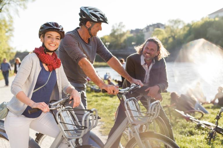 Three cyclists are standing and talking to each other at the Isar River in Munich.