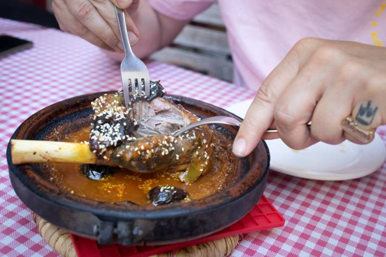 Someone is cutting a lamb shank with two forks.