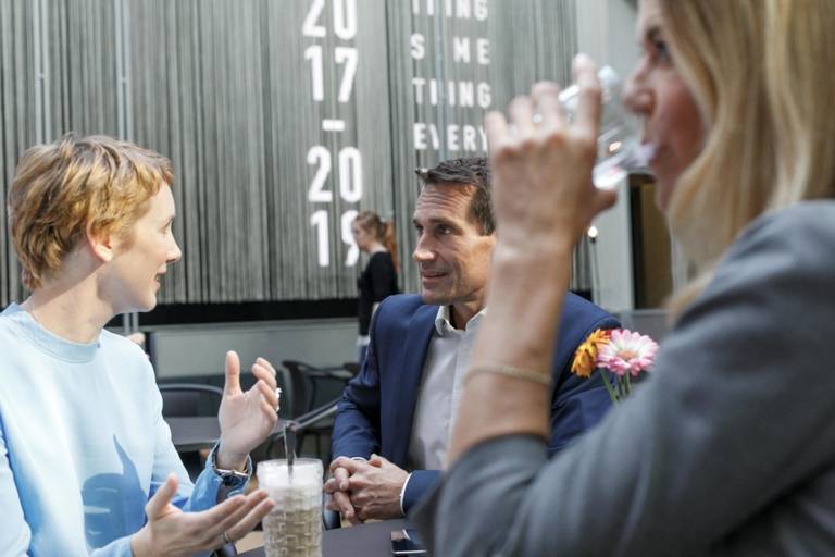 Two women and a man are talking to each other in the foyer of a hotel in Munich.