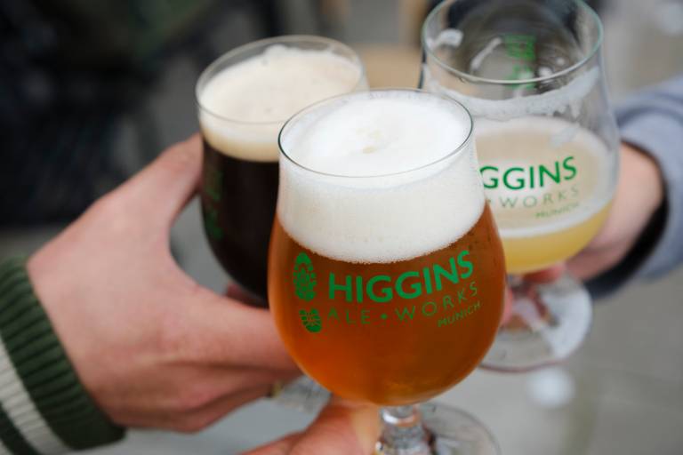 Three people, of whom only their hands can be seen, toast each other with three different coloured beers.