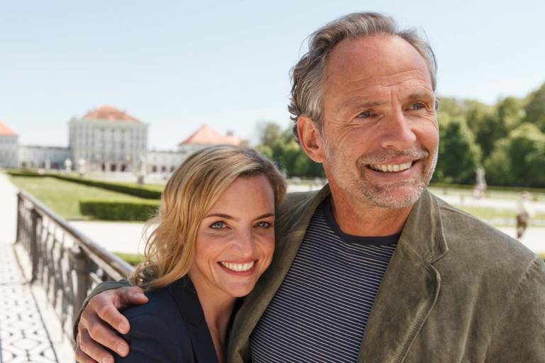 A couple is hugging each other and smiling in front of Nymphenburg Palace in Munich.