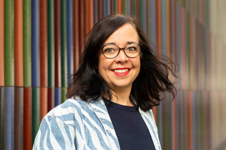 Munich Ambassador Laura Schieferle laughs into the camera and stands in front of the colourful exterior façade of the Brandhorst Museum.