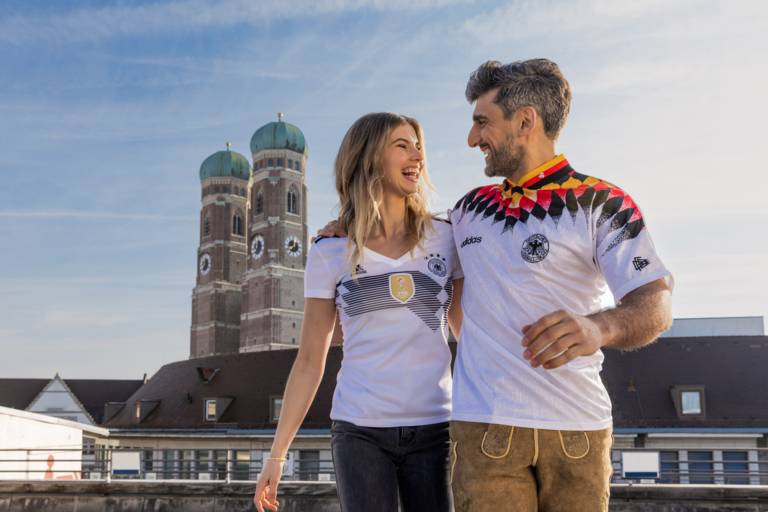 Two football fans wear Germany shirts in Munich and the towers of the Frauenkirche can be seen in the background.