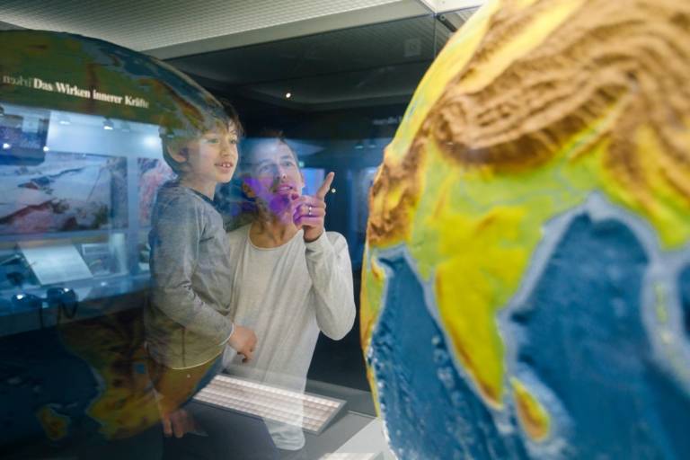 Un homme montre du doigt le globe terrestre dans la vitrine du Musée de l'Homme et de la Nature à Munich et le montre à son garçon qu'il porte dans ses bras.