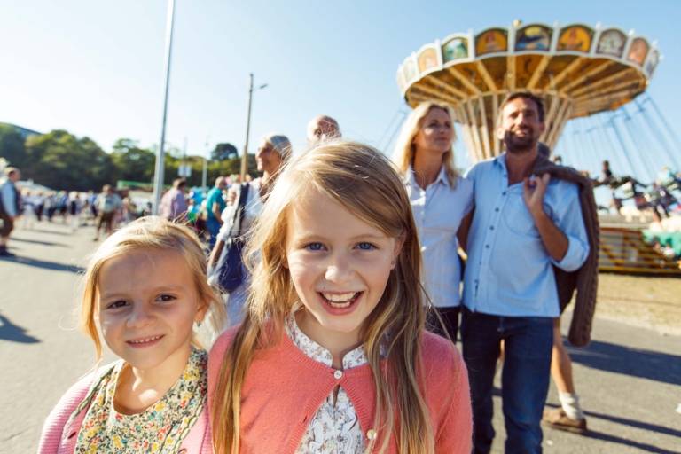 Two blonde girls are strolling with their parents through the Oktoberfest in Munich.