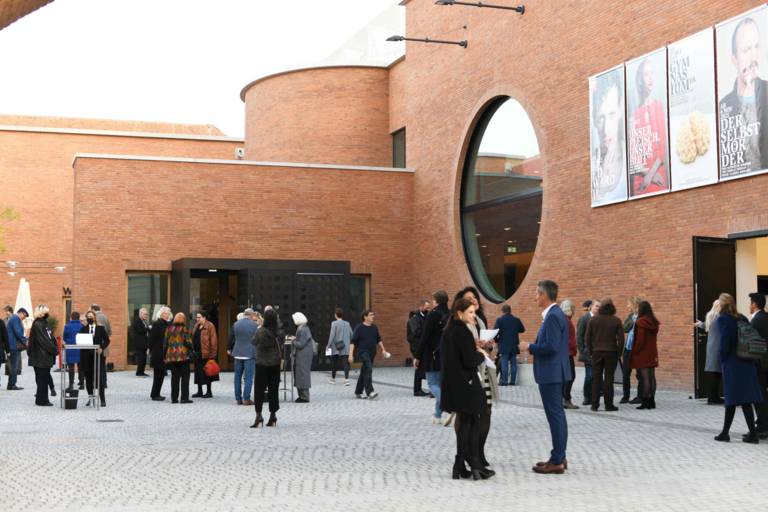 Theatre-goers linger in the courtyard of a brick-fronted theatre before the performance.