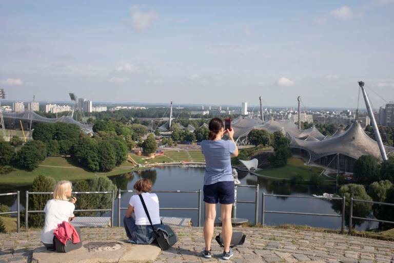 Tre turisti sulla piattaforma panoramica dell'Olympiaberg con vista sul parco e sull'entroterra.