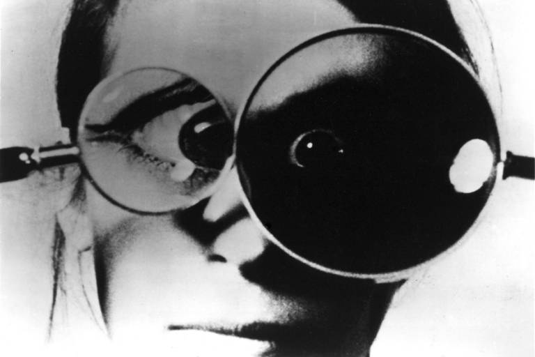Black and white photo of a woman holding two magnifying glasses in front of her eyes.