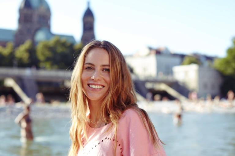 A young woman is standing in front of the Isar River in Munich on a sunny day.