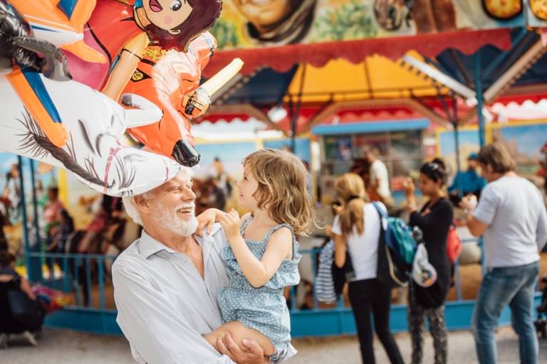 A grandfather is carrying his granddaughter in his arms at the Auer Dult in Munich.