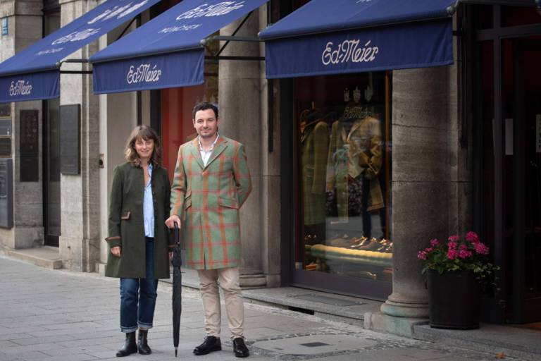 A woman and a man in a coat in front of the shop of Eduard Meier in Munich