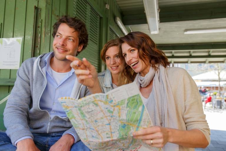 A woman is holding a city map in her hands and is giving a direction to a couple at the Viktualienmarkt in München.