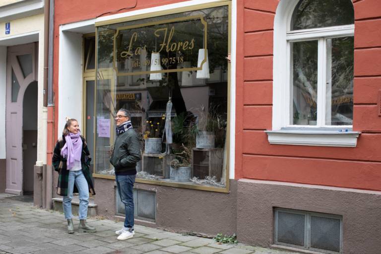 A man and a woman stand in front of a flower shop in autumn and talk.