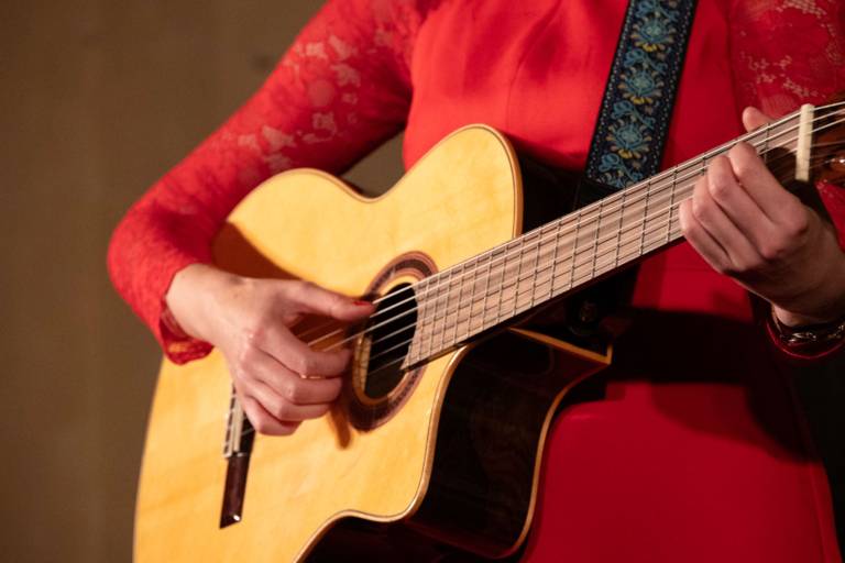 Cabaret artist Claudia Pichler stands on a stage and plays a guitar.